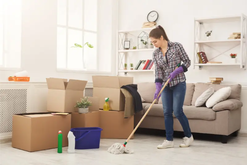 young female professional mopping floor surrounded by moving boxes during move out cleaning