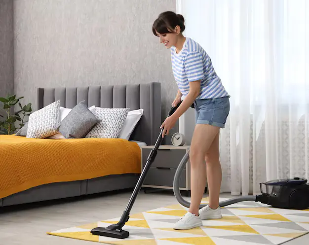 Young woman professional vacuuming carpet in the bedroom during house cleaning services in Ajax