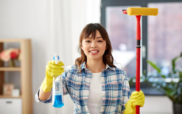 Young and happy woman professional cleaner holding cleaning spray and mop during house cleaning services in Mississauga and Brampton