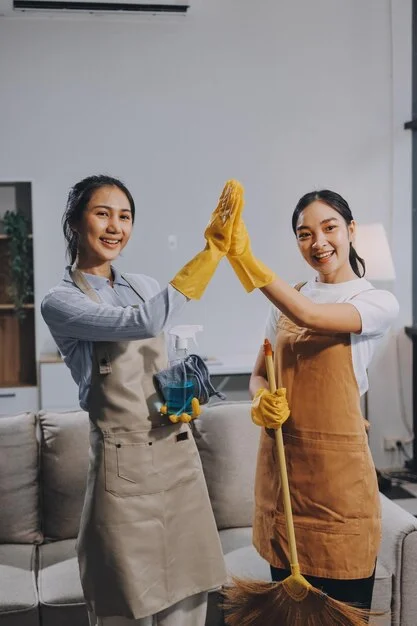 Two happy female professionals giving high five to each other after successful cleaning services in Whitby